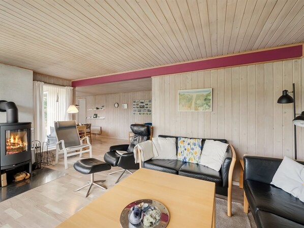 A cozy living room with a fireplace, leather sofas, a wooden coffee table, and a dining area with chairs.