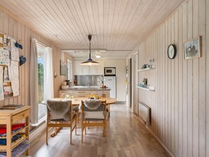 Une cuisine avec des panneaux de bois au mur, un coin repas avec des chaises, un luminaire suspendu et une horloge au mur.