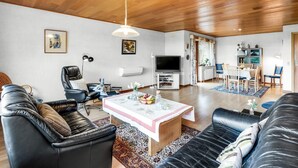 Amplia sala de estar con techo de madera, un sofá de cuero negro, zona de comedor con mesa y sillas, y televisor.