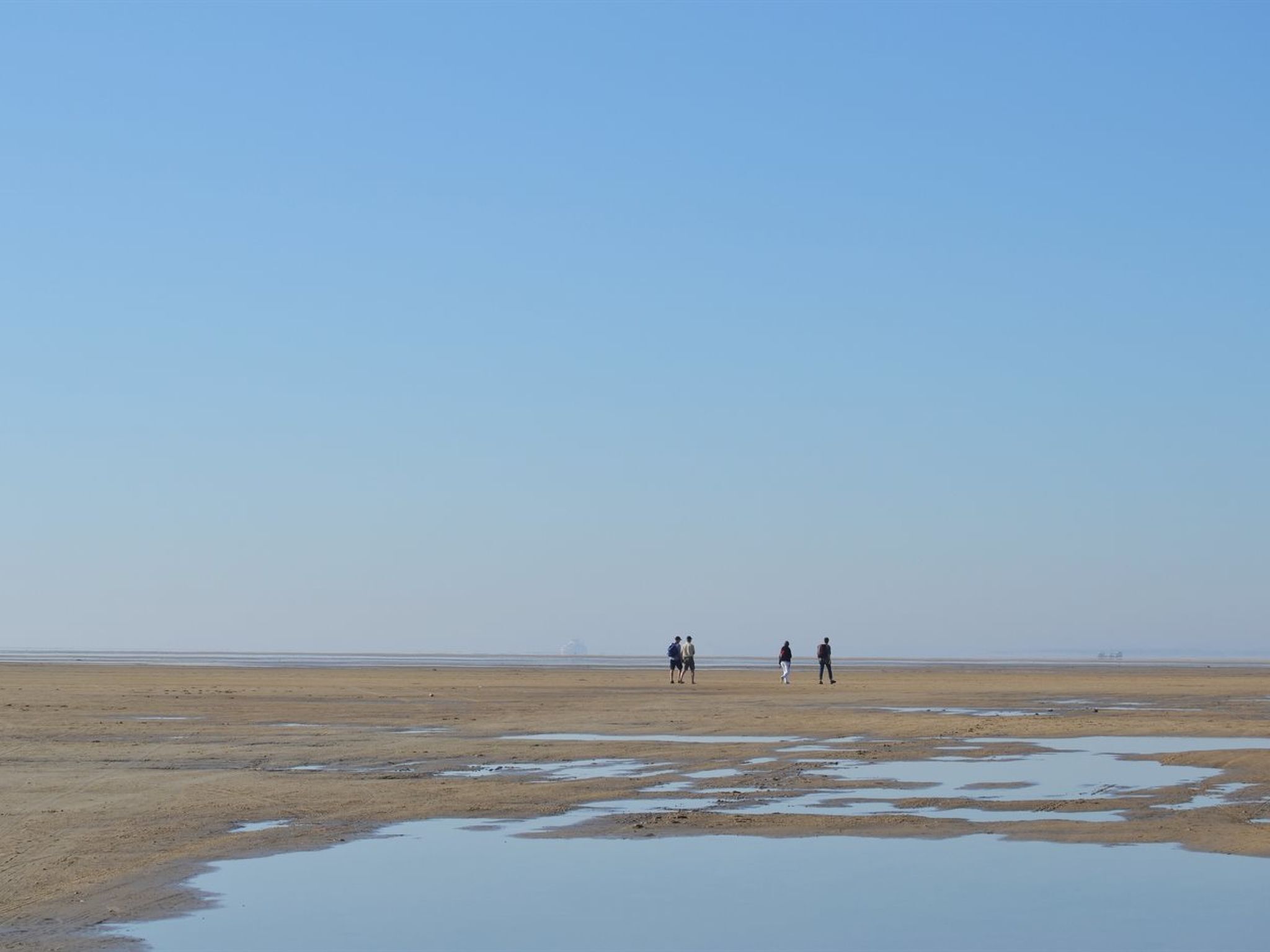 A wide, open beach with a few people walking.