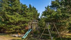 A playground with a slide and swings, surrounded by trees.