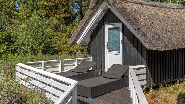 A small cabin with a thatched roof, a wooden deck, and two lounge chairs.