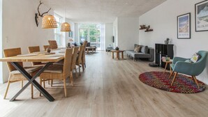 Ein geräumiger Wohnbereich mit Esstisch, Korbstühlen, einem grauen Sofa und einem farbenfrohen Teppich.