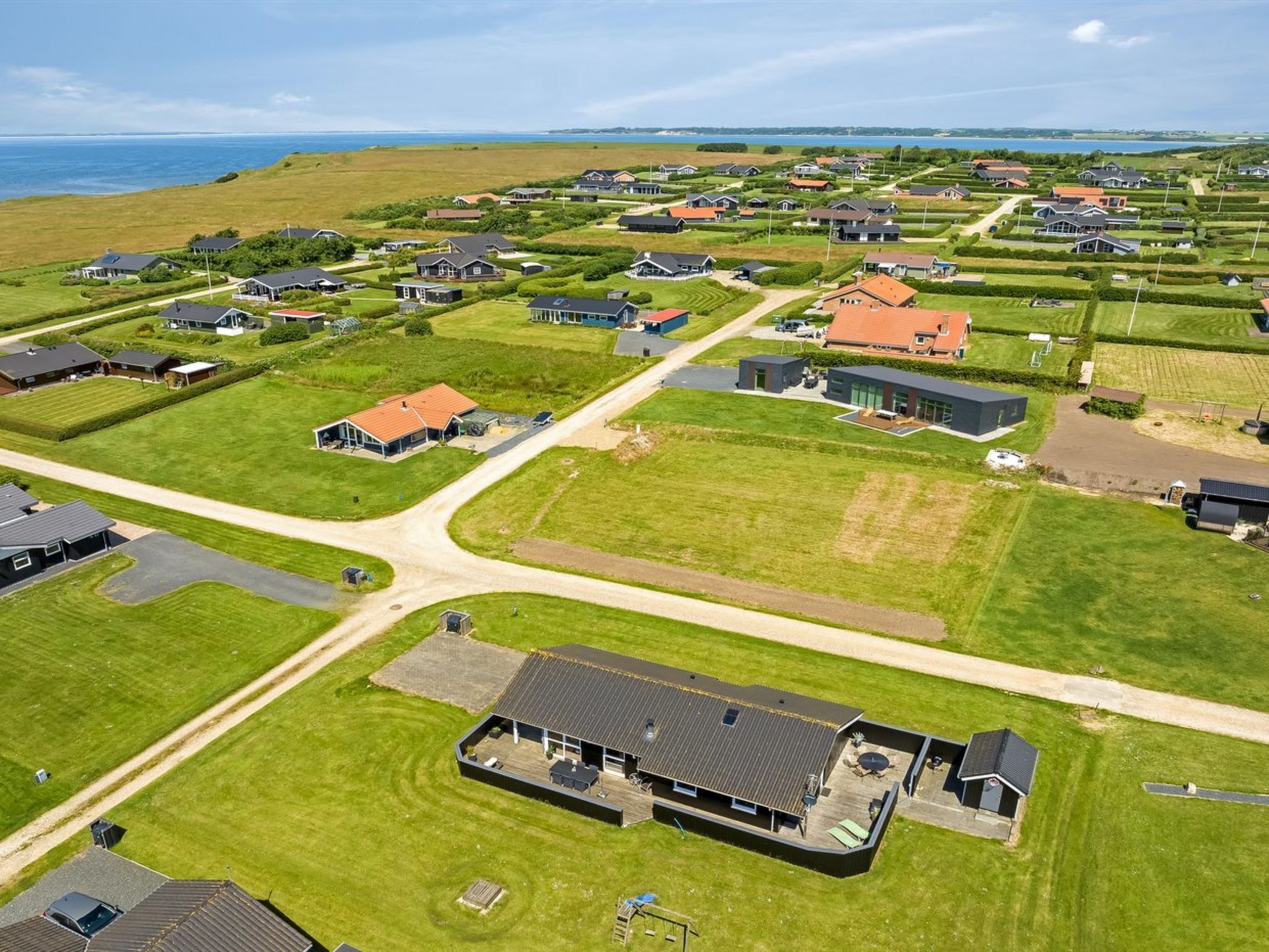 Ett flygbildsbild av ett bostadsområde med hus, grönskande gräsmattor och en stor vattenyta i bakgrunden.