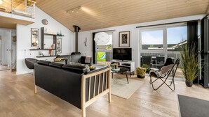 A modern living room with a black sofa, a TV, and a dining area with chairs. - "Samuil" - 300m to the fjord by Interhome (Vinderup)