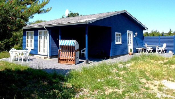 Una casa azul con porche cubierto, mobiliario exterior y una pequeña mesa.