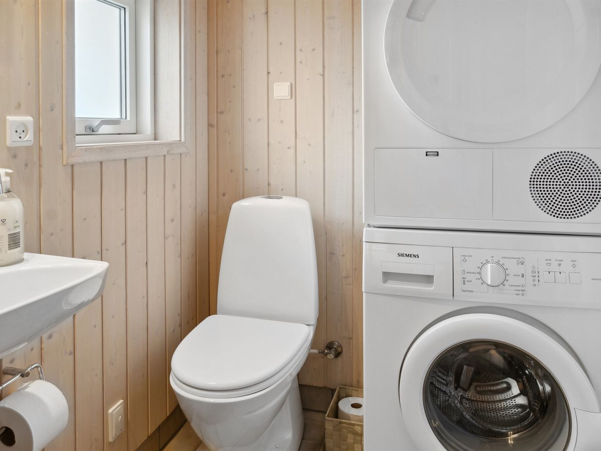 A compact bathroom with a toilet, sink, and a stacked washer and dryer unit.