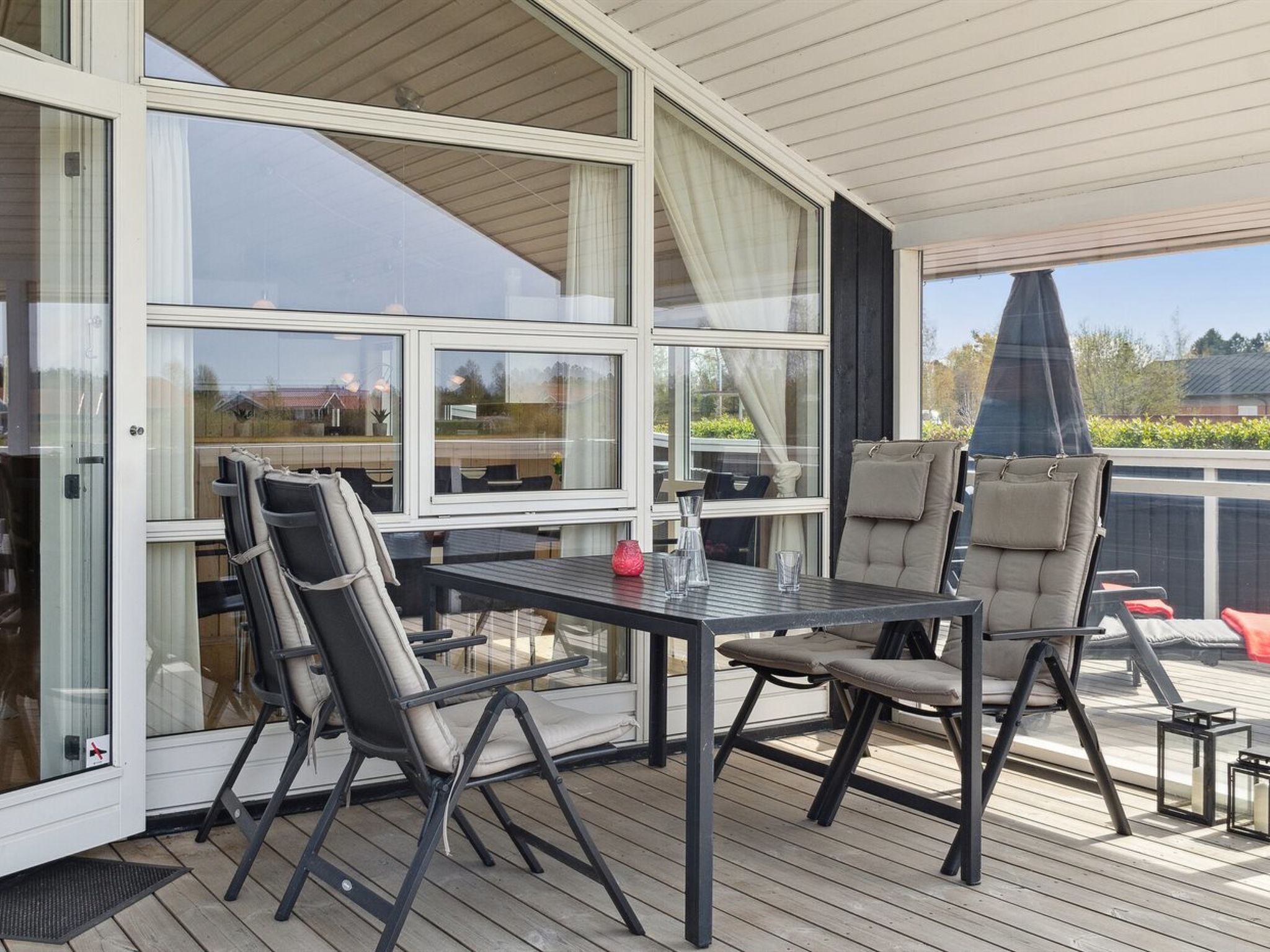 A covered outdoor patio with a table and chairs, large windows, and a view of the surrounding area.