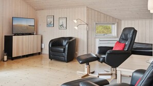 Un salon moderne avec un plafond en bois, un téléviseur à écran plat, un canapé en cuir noir, un fauteuil en cuir noir et une petite table.