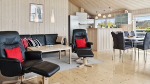 Un salon moderne avec un canapé en cuir noir, une table à manger avec des chaises et un coin cuisine doté de meubles en bois et de luminaires suspendus.