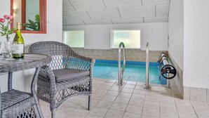 Un área de piscina con una silla de mimbre, una mesa con una botella y vasos, y un ventanal con vista a la piscina.