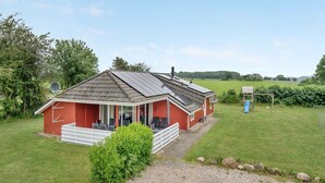 Una casa roja con un porche cubierto, paneles solares y un jardín pequeño.