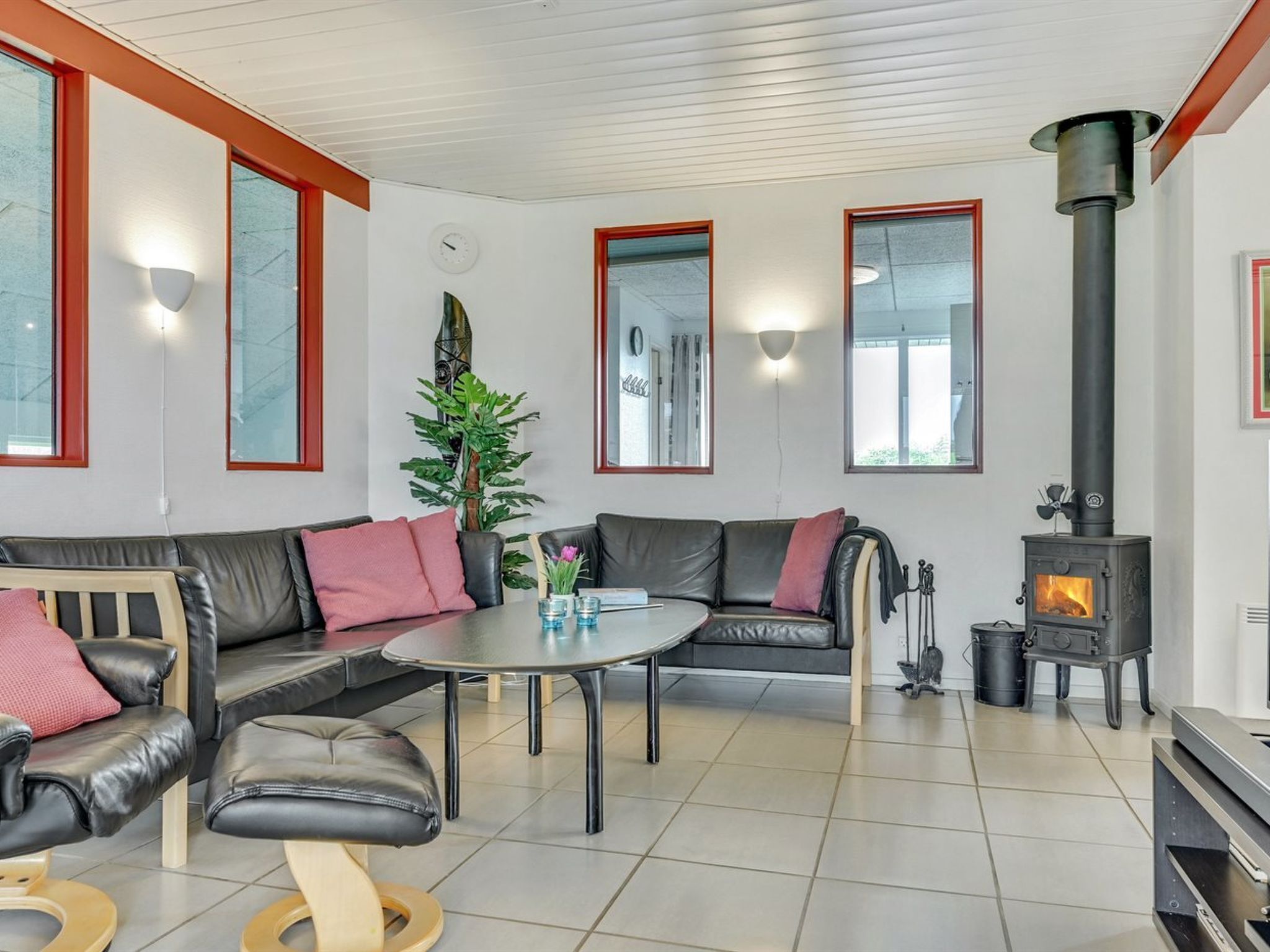 Un salon moderne avec un canapé en cuir noir, une table ronde et un poêle à bois noir.