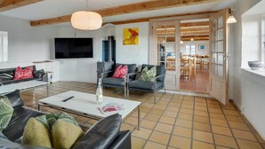 A spacious living area with a high ceiling, exposed wooden beams, a large television, and a dining area visible through an open door. - "Answald" - 250m from the sea by Interhome (Harboøre)