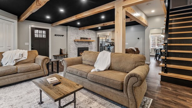 Una sala moderna con chimenea, vigas de madera y una cocina al fondo.