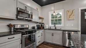Una cocina moderna con electrodomésticos de acero inoxidable, armarios blancos, un ventanal grande y techo negro.