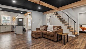 Una sala de estar moderna con un sofá seccional marrón, una pequeña mesa de madera y una escalera que conduce a otro nivel.