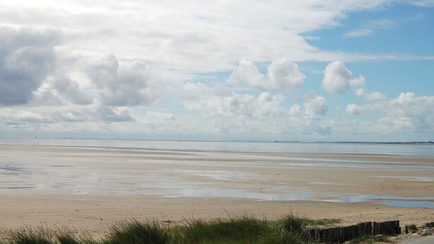 Ein Strand mit weitem, feuchtem Sand und einem Holzzaun im Vordergrund.