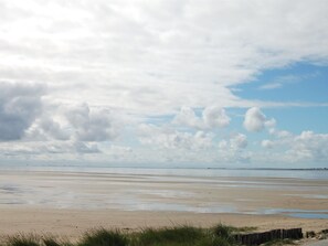 Ein Strand mit weitem, feuchtem Sand und einem Holzzaun im Vordergrund.