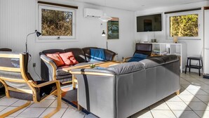 Ein modernes Wohnzimmer mit einer Couch, Sesseln, einem Fernseher und Kunstwerken an den Wänden.