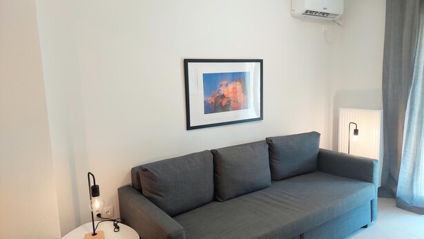 A modern living room with a grey sofa, a framed picture on the wall, a lamp, and a radiator. - Modern Apartment in Acropolis Museum (Athens)