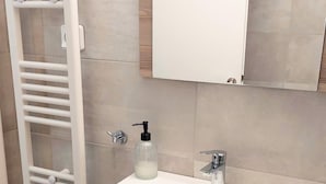 A bathroom with a white vanity, a mirror, a towel rack, and a soap dispenser. - Modern Apartment in Acropolis Museum (Athens)