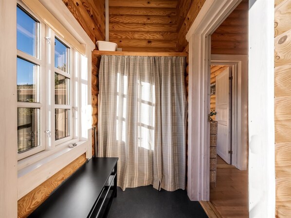 A room with wooden walls, a black bench, a window with blinds, and a door leading to another room.