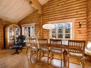 Ein rustikales Blockhaus-Interieur mit Essbereich, Holzwänden und großen Fenstern.