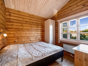 Ein Schlafzimmer in einer Blockhütte mit einem Bett, einem Fenster und einer kleinen Küche.