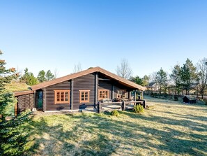 Eine Blockhütte mit Veranda, umgeben von einer grünen Wiese und Bäumen.