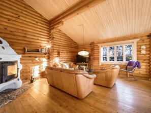 Een blokhut interieur met een open haard, leren banken, een televisie en een groot raam.