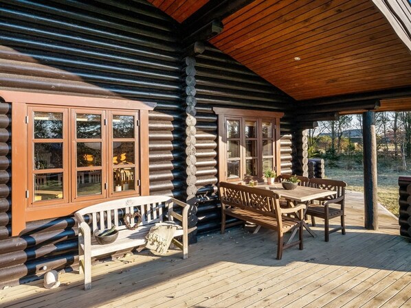 Een vakantiehuisje van hout met een houten terras, een bank en een tafel met stoelen.