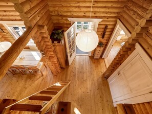 A wooden interior with a staircase, a hanging light fixture, and a view through an open door.