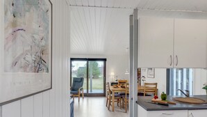 A modern kitchen with white cabinetry, a dining area with a table and chairs, and a large window providing a view of the outdoors. - "Aileen" - 900m from the sea by Interhome (Væggerløse)