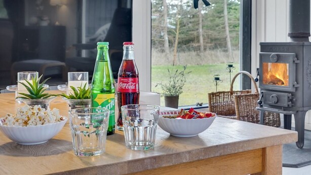 A cozy living room with a wooden table set with snacks, drinks, and a fireplace. - "Aileen" - 900m from the sea by Interhome (Væggerløse)