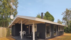 A small, dark-colored cabin with a covered porch and a chimney. It has a seating area with chairs and a table. - "Aileen" - 900m from the sea by Interhome (Væggerløse)