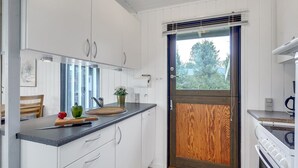A compact kitchen with white cabinets, a wooden door, and a window overlooking greenery. - "Aileen" - 900m from the sea by Interhome (Væggerløse)