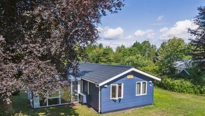 A small, single-story house with a blue exterior and a sloped roof, surrounded by a grassy yard and trees. - "Winona" - 300m from the sea by Interhome (Væggerløse)