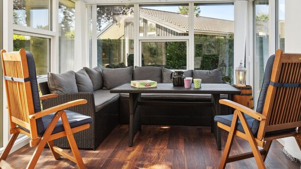 A sunroom with a large glass enclosure, a sectional sofa, two wooden chairs, a small table, and a lantern. - "Winona" - 300m from the sea by Interhome (Væggerløse)