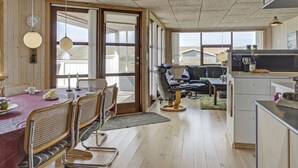 Een gezellige, open leef- en eetruimte met een houten vloer, een eettafel met stoelen, een bank en een keukenhoek met een magnetron en een klein eiland.