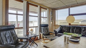 Een kamer met een groot raam, een houten tafel, twee leren stoelen, een bank en een lamp.