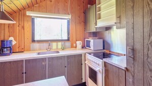 A compact kitchen with wooden cabinets, a sink, a stove, a microwave, and a window providing natural light.