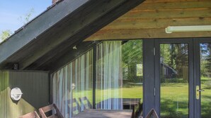 A covered outdoor seating area with a wooden table and chairs, a glass door leading to a grassy yard, and a wooden ceiling structure.