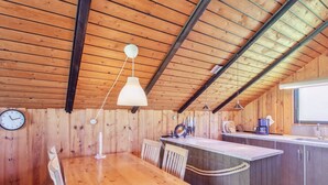 A wooden interior with a dining table, chairs, a kitchen island, and a clock on the wall.
