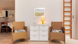 Une pièce comprenant deux fauteuils en osier, une commode blanche, une lampe jaune et un tableau encadré accroché au mur.