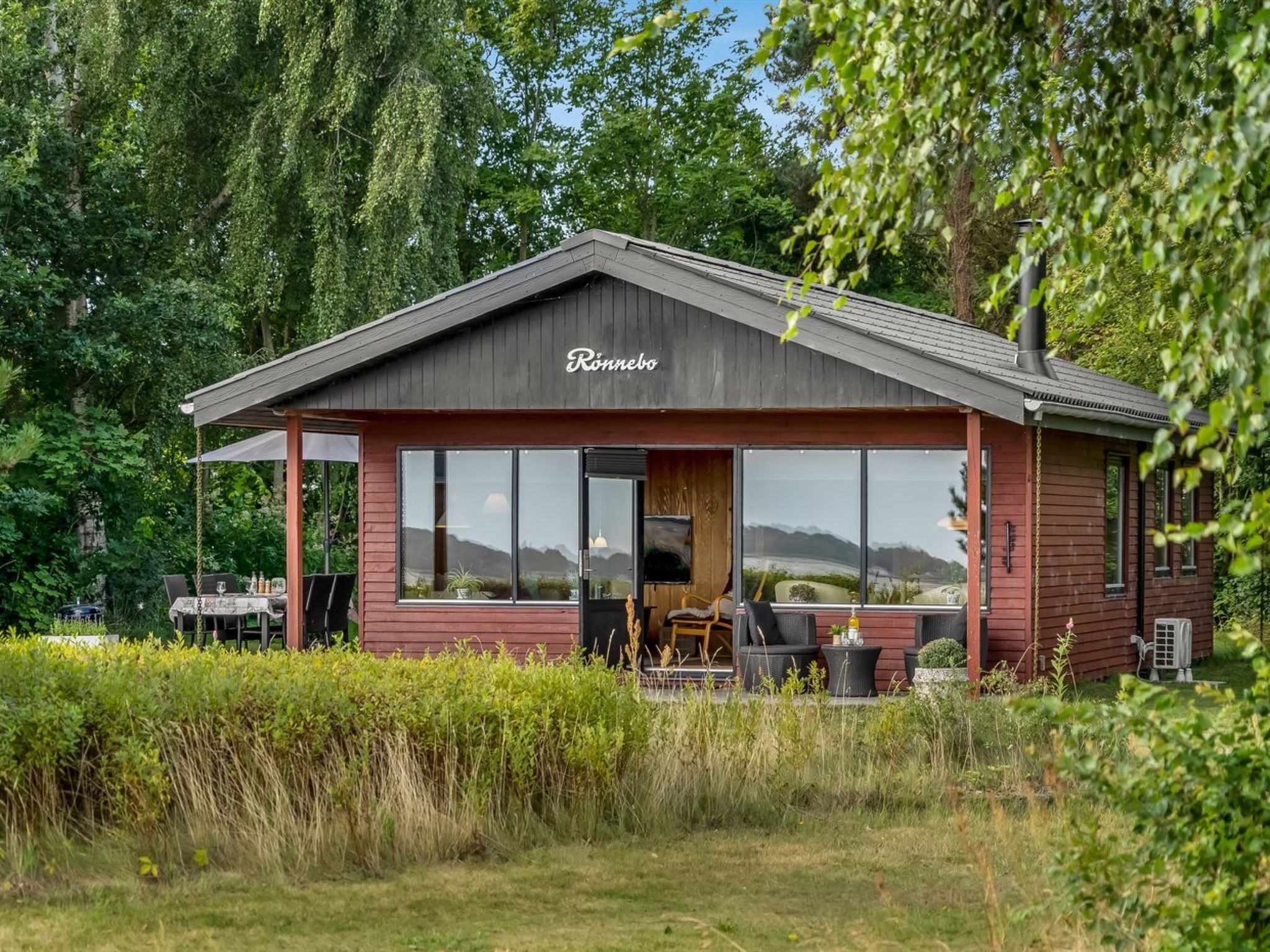 A wooden cabin named 'Ronnenbo' with large windows, a patio area, and a view of the surrounding landscape.