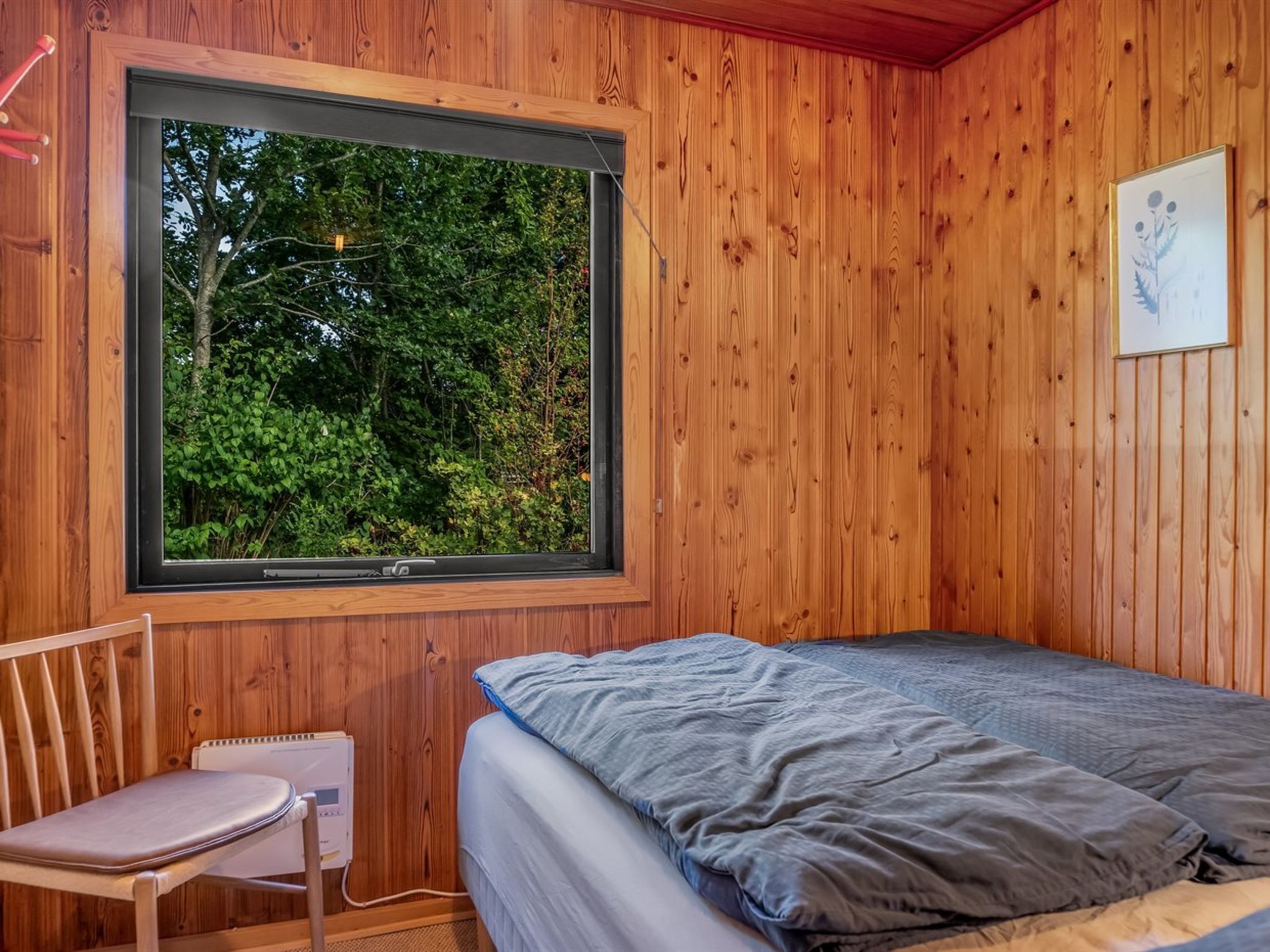 Habitación de madera con una cama, una silla y ventana con vistas a la vegetación.
