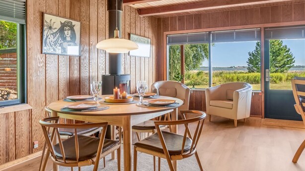 A cozy dining area with a wooden table, chairs, and a large window offering a scenic view. - "Tayana" - 75m to the fjord by Interhome (Storvorde)