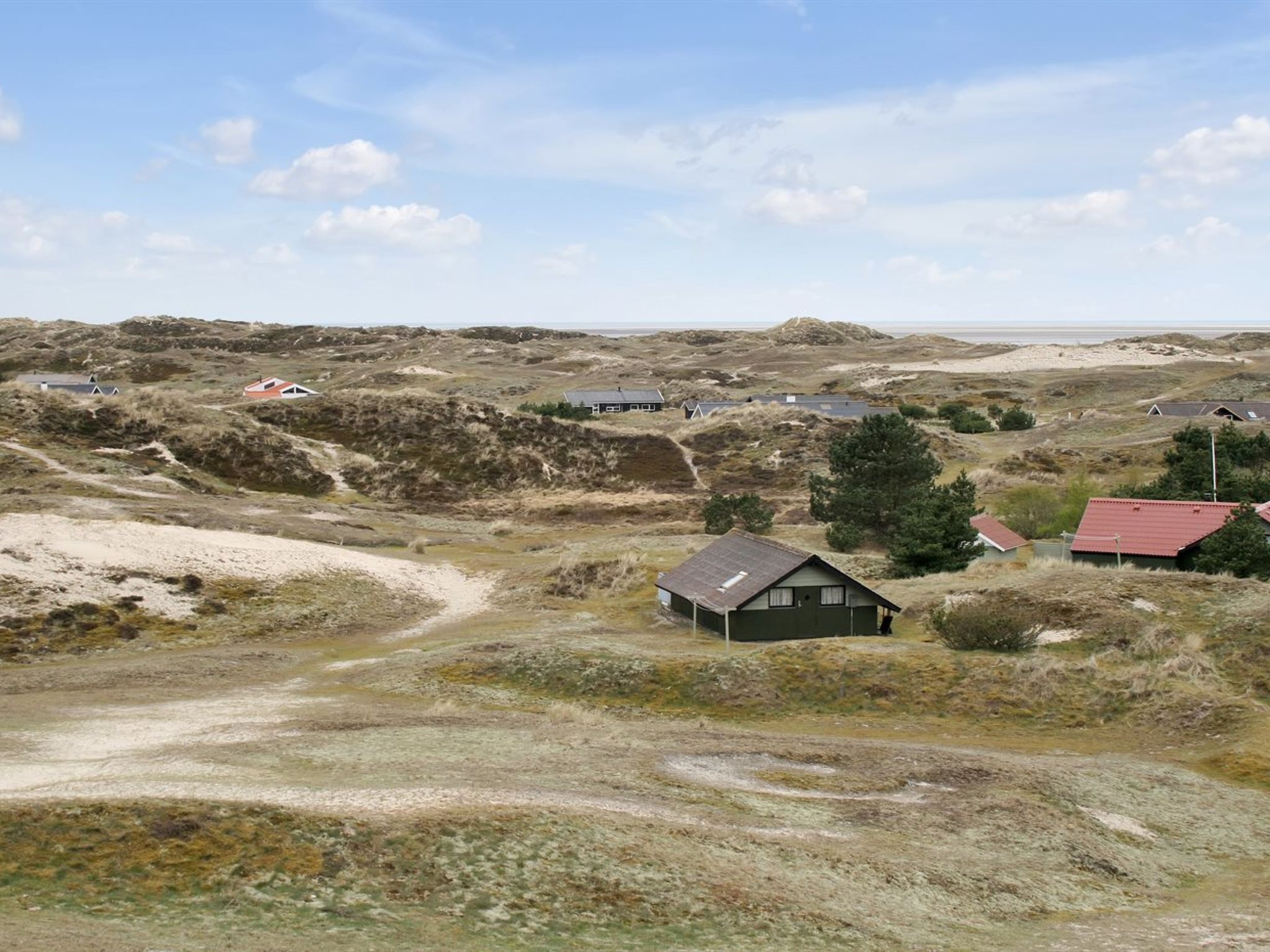 A rural landscape with several houses, a dirt path, and sparse vegetation.