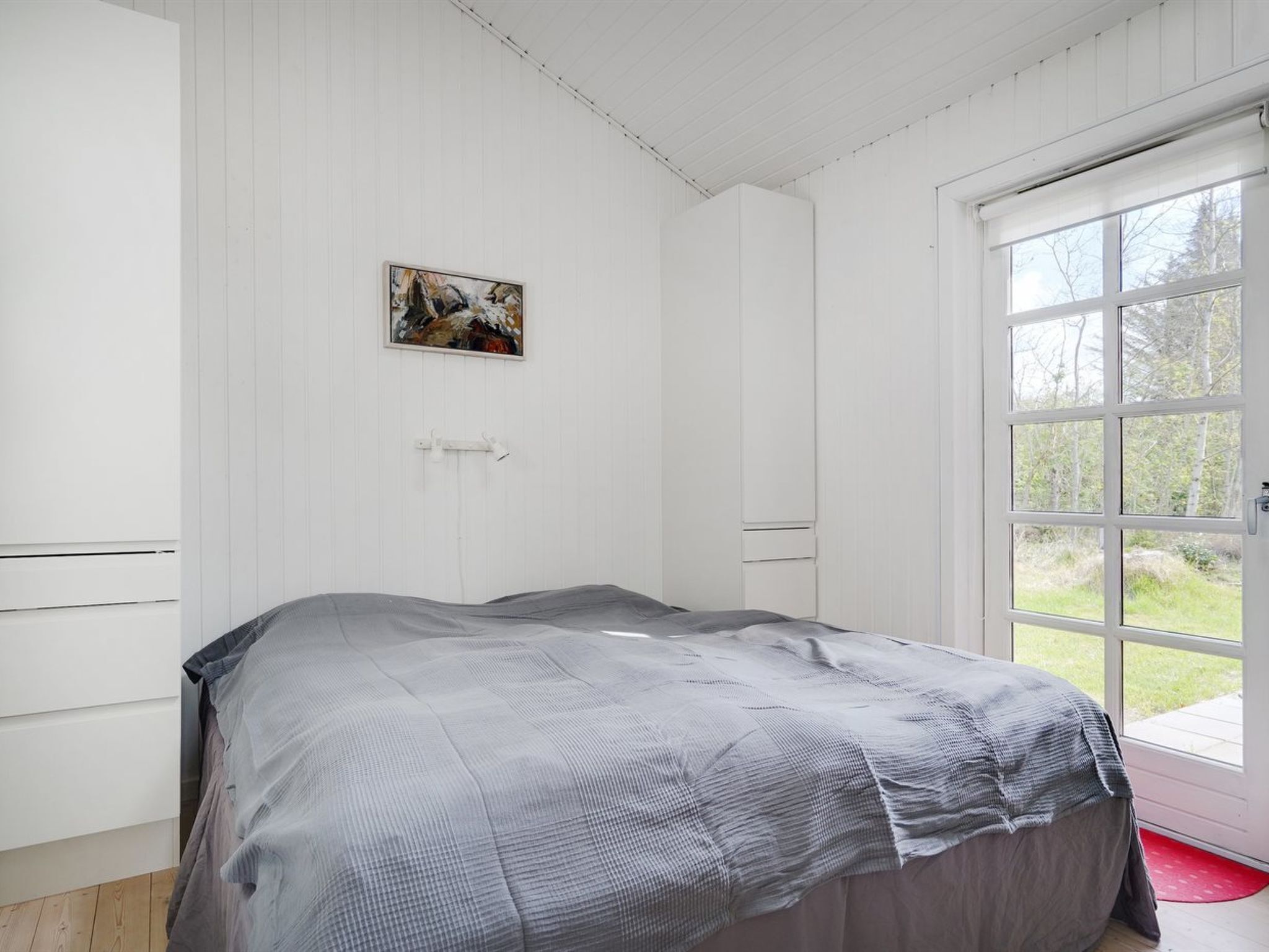 A bedroom with a bed, a door to an outdoor area, and a painting on the wall.
